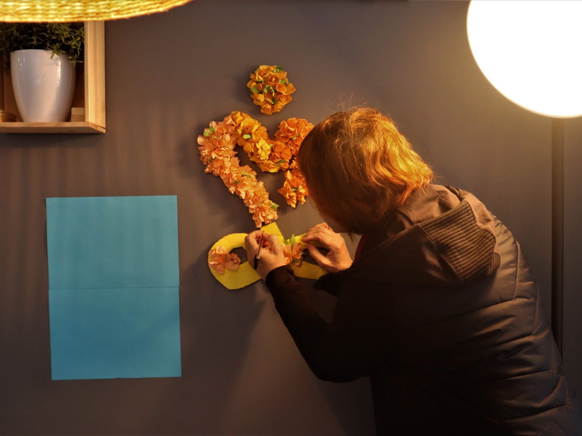 Persona haciendo un corazon con flores a mano en una pared